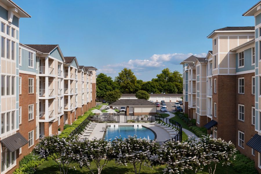 Attain at Greenbrier apartment homes with Apartment buildings surround a courtyard with a swimming pool, lounge chairs, and trees under a clear blue sky.