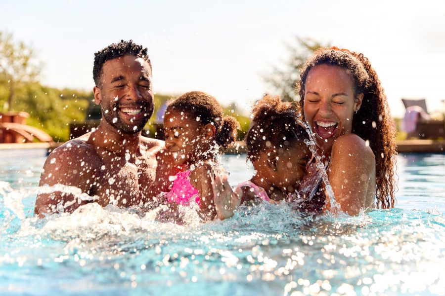 Attain at Greenbrier apartment homes with Smiling family with two young children splashing and playing together in a swimming pool on a sunny day.